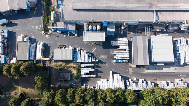 Aerial view of a construction materials manufacturing facility with organized stacks of building supplies, industrial warehouses, and surrounding greenery in Milan, Lombardy, Italy.