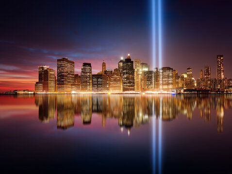 Manhattan skyline during Patriot Day with symbolic twin light beams, blue hour atmosphere, illuminated buildings, respectful commemorative concept.