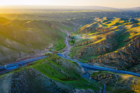 Scenic mountain landscape with a winding highway and rolling green hills illuminated by warm golden sunlight during sunset.
