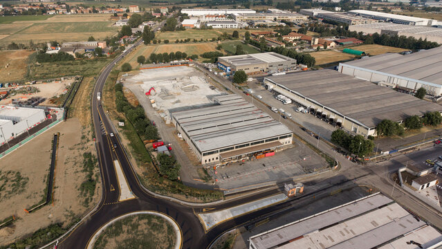 Aerial view of distribution centers in a large industrial zone with warehouses, a construction site, and a roundabout in Siziano, Lombardy, Italy.