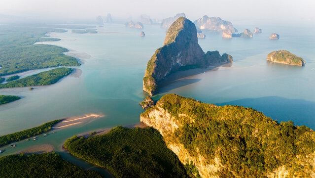 Aerial view of Phang Nga Bay featuring dramatic limestone karst formations rising from turquoise waters, surrounded by lush mangrove forests and calm sea, Thailand.