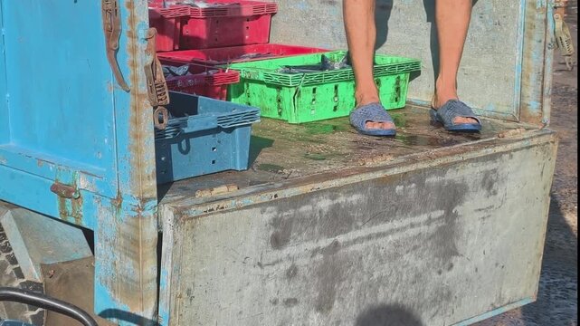Vietnamese traditional three-wheeled truck at a coastal fish market, a worker standing on the vehicle turning around to arrange incoming fresh fish crates
