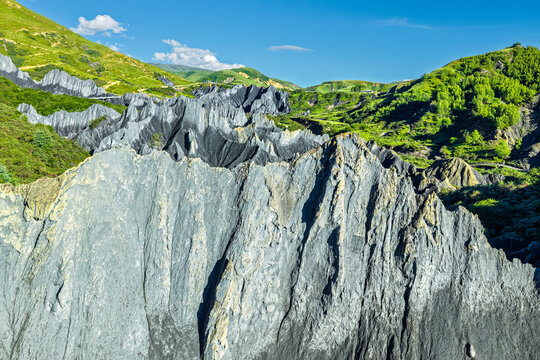 Dramatic gray stone rock formations contrast with green mountain slopes under a clear blue sky in Sichuan, China.