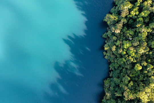 Aerial view of the turquoise and deep blue waters of Lake Eacham bordered by dense tropical rainforest in Atherton Tablelands, Queensland, Australia.