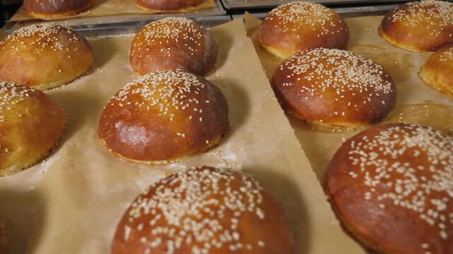A detailed view of freshly baked burger buns with sesame seeds in the kitchen of a restaurant. The buns have a golden-brown exterior and a delightful aroma.