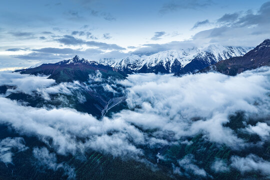 Majestic snow-capped mountain peaks rising above thick sea of clouds in Sichuan, China, creating a serene panoramic natural landscape.