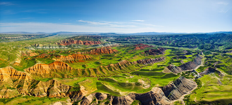 High angle view of colorful Danxia landforms and lush green valleys under a clear blue sky, showing unique geological erosion formations.