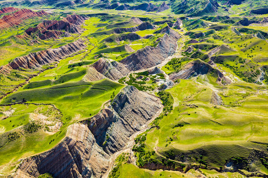 High angle view of vibrant green rolling grassland and eroded colorful mountain landforms showcasing natural geology.