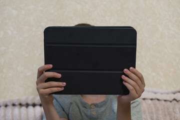 Young boy holding digital tablet sitting on couch at home. Child studying online, playing games or watching video content on modern portable device indoors. Technology and education concept. ( © Тетяна Хіміченко