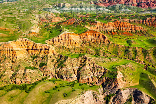 Vibrant colorful Danxia landforms and lush green grassland captured from high above, showing geological beauty and natural erosion patterns.