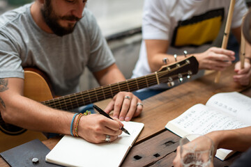 People writing music notes at a table with a guitar and notebook. © Rawpixel.com