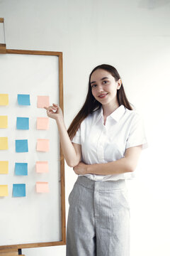 Asian businesswoman standing and pointing to whiteboard with sticky notes for business presentation planning and strategy concept