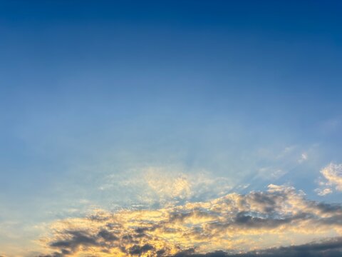 A wide-angle horizontal landscape photograph capturing brilliant crepuscular rays fanning out over a bed of golden-lit clouds against a rich blue sky