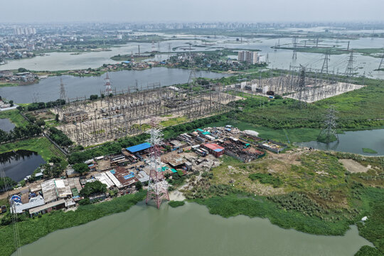 Aerial view of an electrical substation with power lines and transmission towers situated near water bodies and industrial buildings in Dhaka, Dhaka Division, Bangladesh.