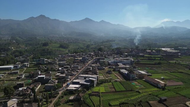 Aerial drone footage of rural village and green vegetable farmland with Mount Panderman background in Pujon, Malang