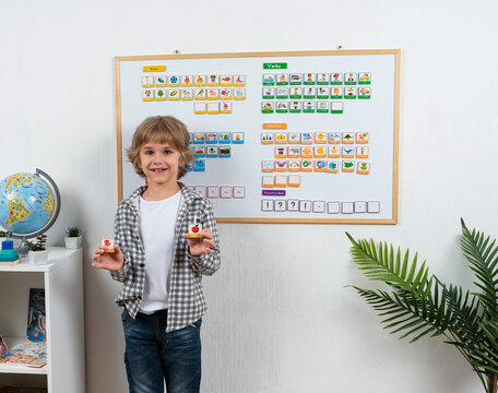 Smiling schoolboy holds colorful picture word cards in front of a magnetic learning board while practicing English vocabulary, grammar and sentence building skills.
