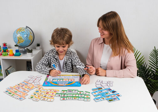 Teacher helps a schoolboy write and build English sentences using colorful word and picture cards at a table during an interactive grammar and language learning activity.