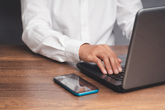 Person using laptop with smartphone on office desk