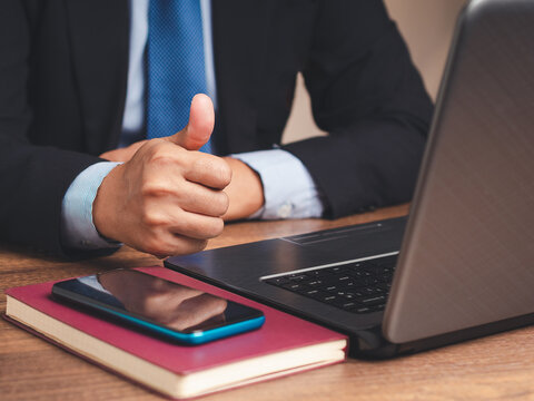 Person giving thumbs up beside laptop and smartphone