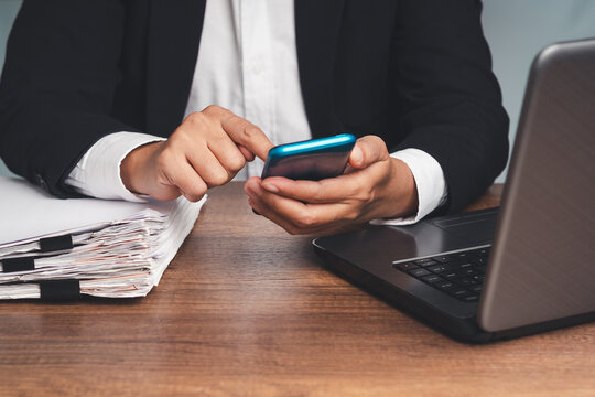 Person using smartphone beside laptop and paperwork