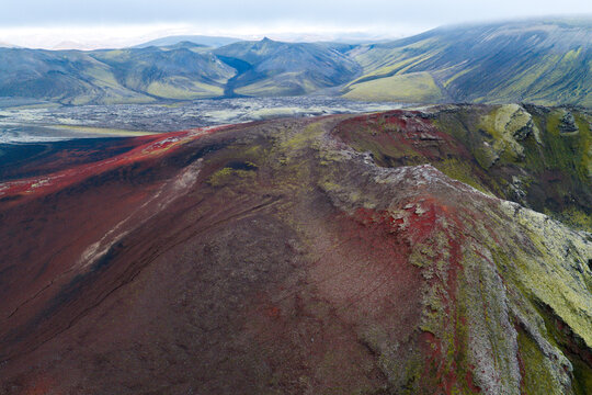 Aerial view of Fjallabak Nature Reserve featuring vibrant red volcanic soil and green mossy slopes in the rugged highlands of Rangarthing ytra, Iceland.