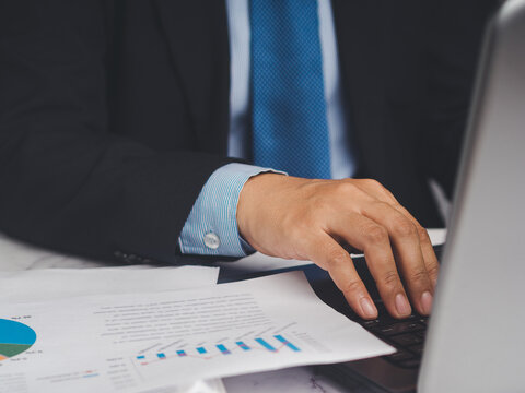 Person using laptop with printed charts on desk