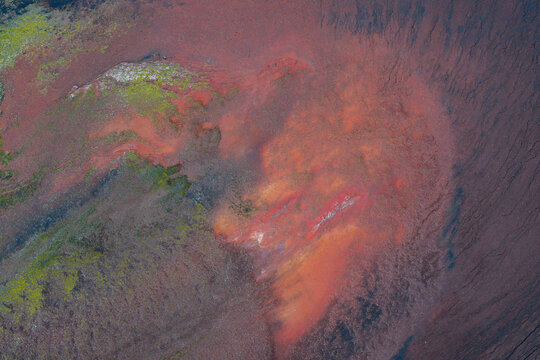Aerial view of the vibrant red and orange volcanic terrain of Fjallabak Nature Reserve, featuring mossy green patches and dark basaltic soil textures in Rangarthing ytra, Iceland.