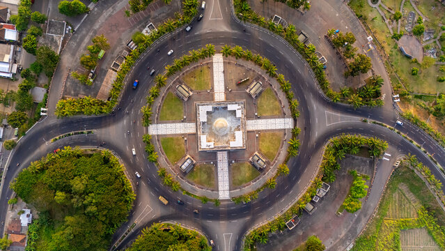 Aerial view of Simpang Lima Gumul monument with its central dome and surrounding circular road intersection, lush green lawns, and palm trees in Kediri, East Java, Indonesia.