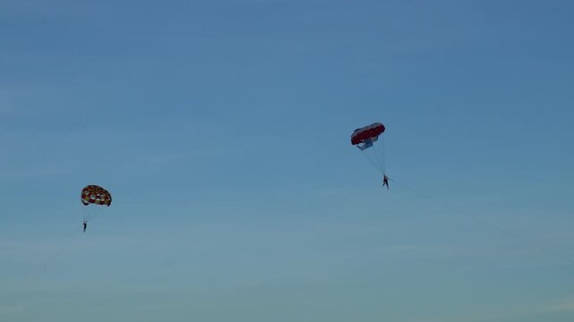 Two parasailers flying colorful parachutes in a clear blue sky