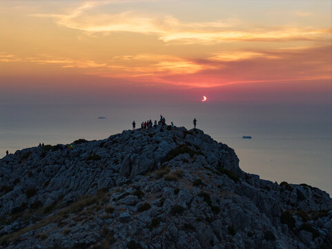 Aerial view of total solar eclipse seen from the rocky summit of Puig de Galatzo in Mallorca with people watching the celestial event against a golden sunset sky Spain.