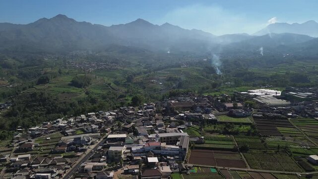 Aerial drone footage of rural village and green vegetable farmland with Mount Panderman background in Pujon, Malang