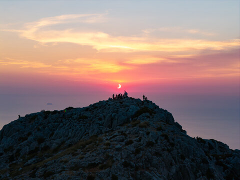 Aerial view of the partial solar eclipse over the rocky summit of Puig de Galatzo with silhouetted people watching the sunset in Spain.