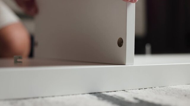 Low angle close up of male hands aligning wooden shelf panel onto sticking screw bolt during furniture assembly