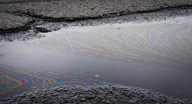 Oil slick with rainbow colors on wet asphalt road after rain. Petroleum pollution floating in water puddle. Environmental contamination from fuel leak. Industrial accident and water pollution concept.
