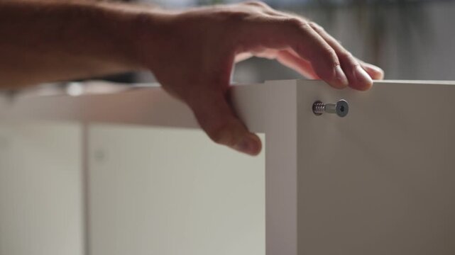 Close up of male hands placing a bolt and tightening it with a socket wrench while assembling wooden shelf