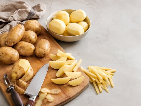 Raw potatoes on a wooden cutting board with a knife and peeler for cooking preparation