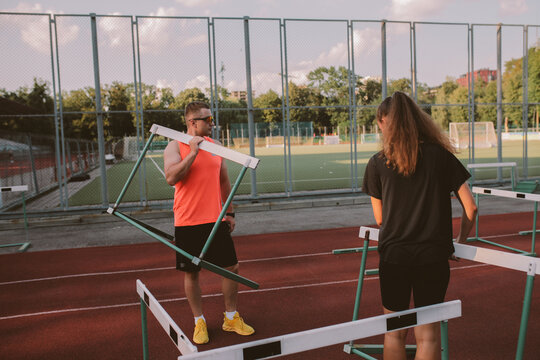 Female athlete training with male coach on hurdles at outdoor stadium
