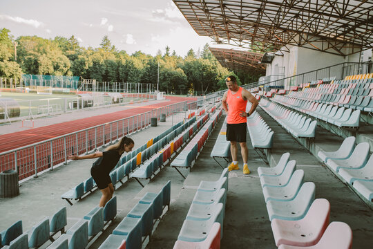 Female athlete training with male coach on hurdles at outdoor stadium