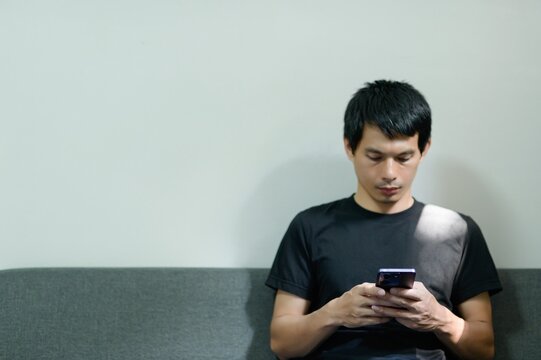 Young Man with Smartphone Relaxing on Couch in Modern Interior Space