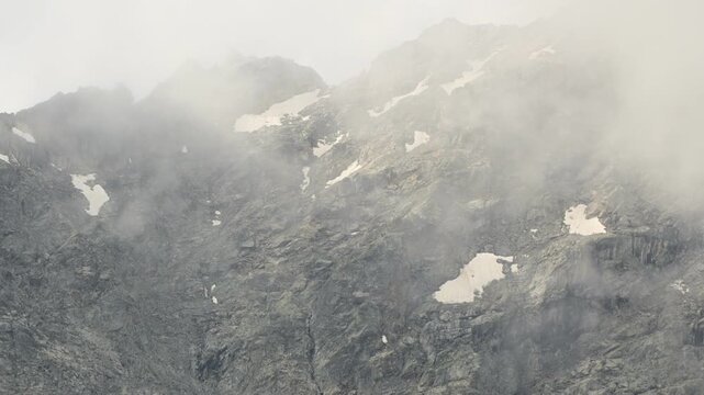 Dense fog rolling across a steep rocky mountain face