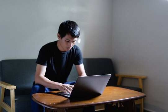 Young Man Working on Laptop at Home with Focused Expression