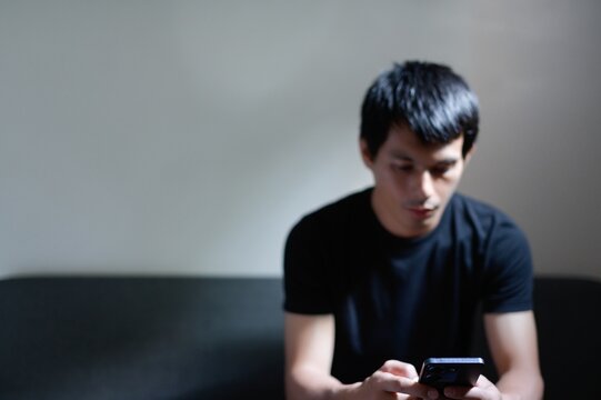 Young Man Using Smartphone in Dimly Lit Room, Casual Pose