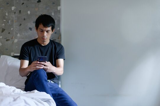 Young Man Engaged with Smartphone in Minimalist Bedroom Setting