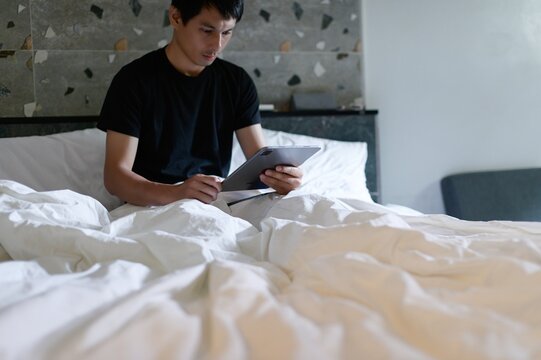Young man using tablet while relaxing on comfortable bed in room