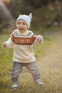 Laughing kid boy 1 year old wearing knitted sweater and hat walking in autumn park. Childhood.