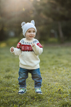 Funny kid boy 1 year old wearing knitted sweater and hat walking in autumn park. Childhood.
