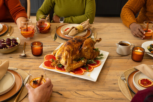 African American family sitting around wooden dining table sharing roasted turkey on white platter