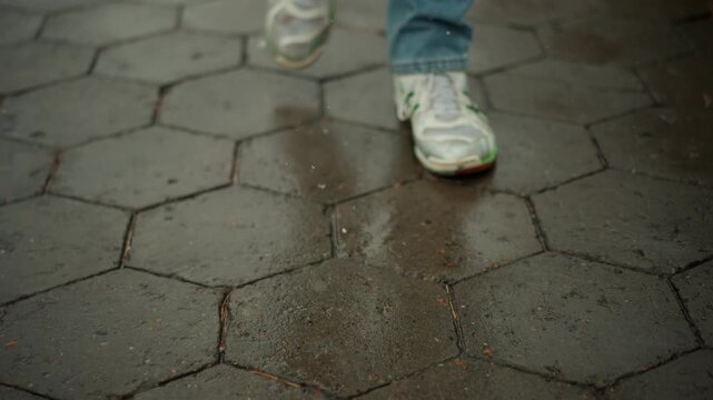 Close up of person feet in white sneakers with green accents walking on wet hexagonal stone pavement. shoes show signs of wear and scene captures continuous foot movement across multiple