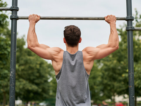 Back view of muscular man doing pull-ups on horizontal bar in outdoor park