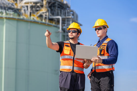 Engineers with laptop pointing and discussing project at industrial plant, Industrial workers team holding computer and checking facility outdoors, Professional plant operators collaborating on site